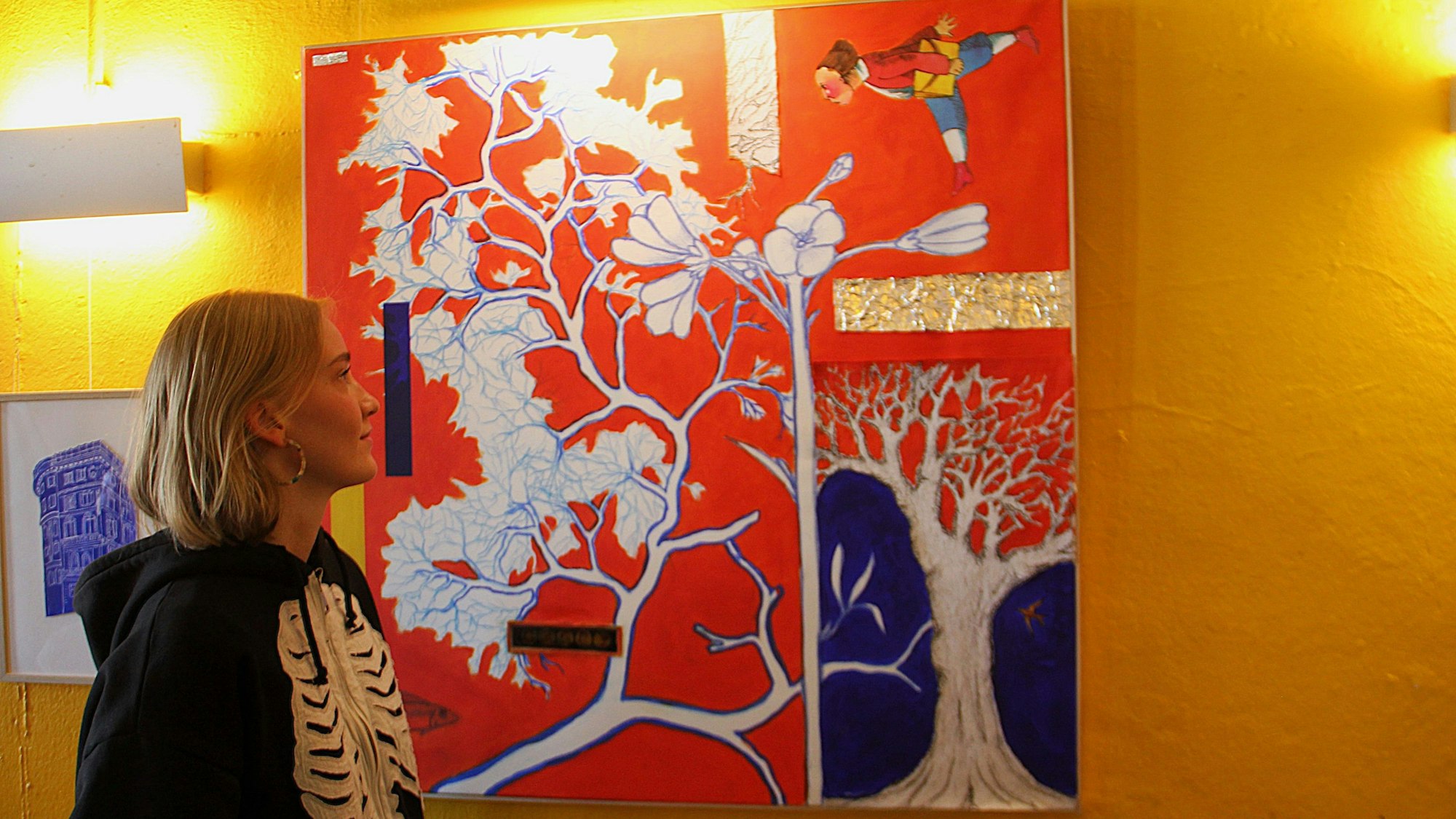 Eine Frau schaut auf ein rot-buntes Bild an einer gelben Wand.