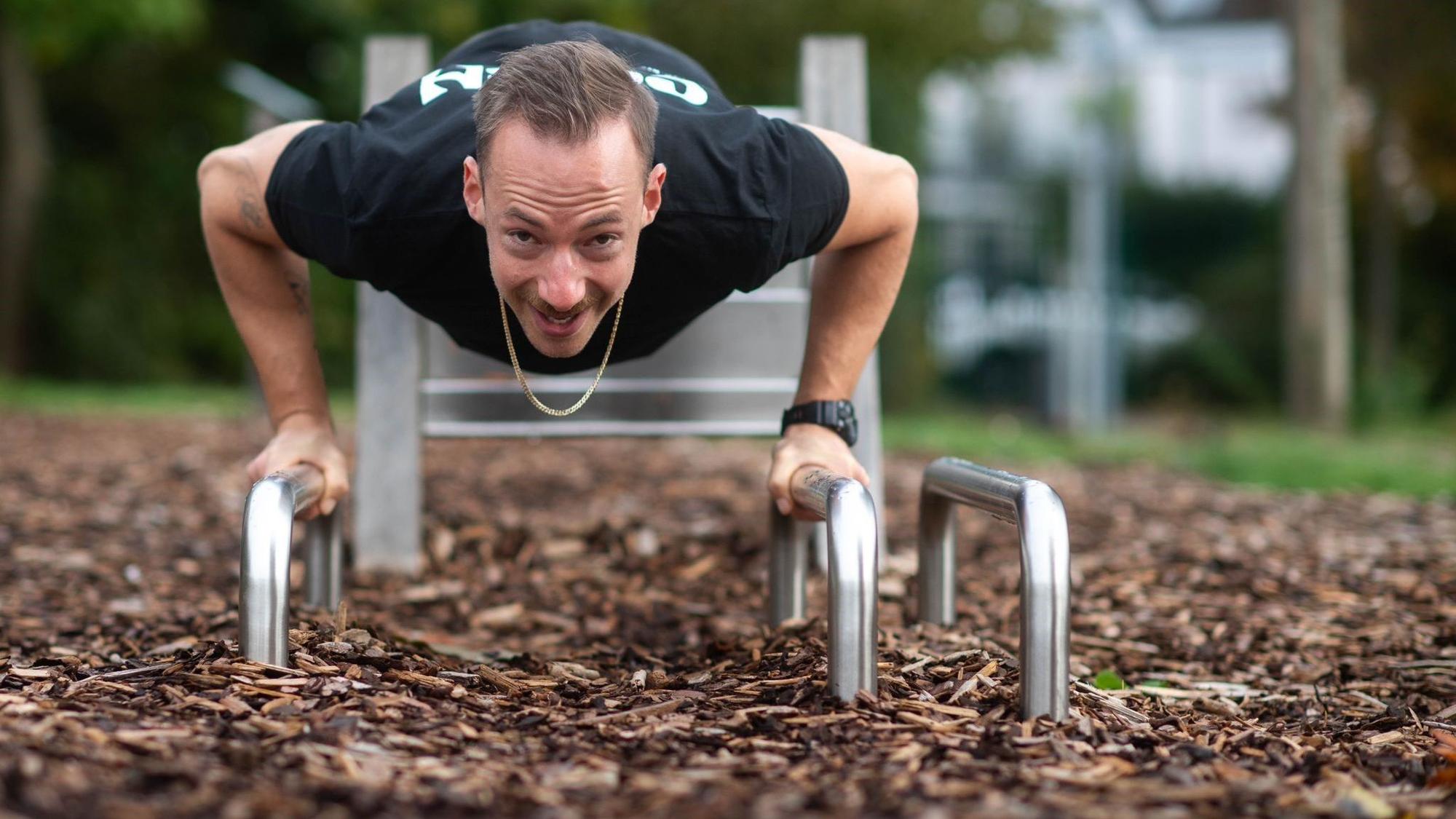 Ein Mann trainiert an einem Fitnessgerät in einem Park.