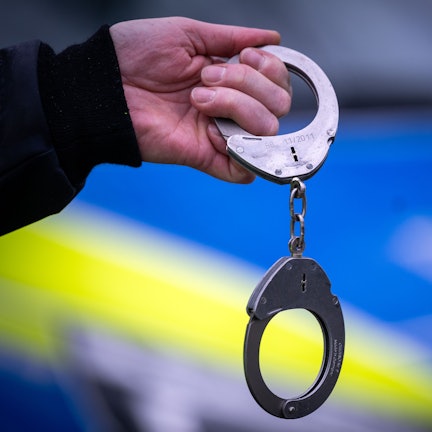 Ein Polizist hält ein Paar Handschellen. (Symbolbild)
