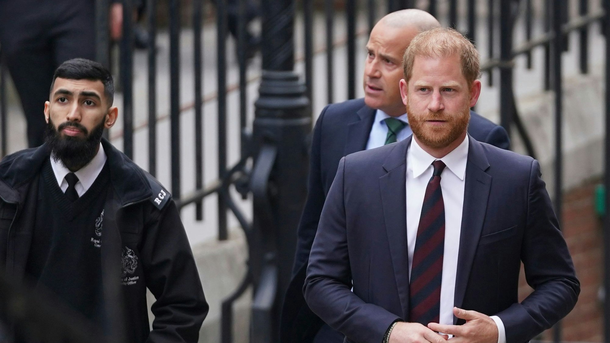 Prinz Harry (r) wird von Sicherheitskräften eskortiert, als er am Royal Courts of Justice eintrifft.