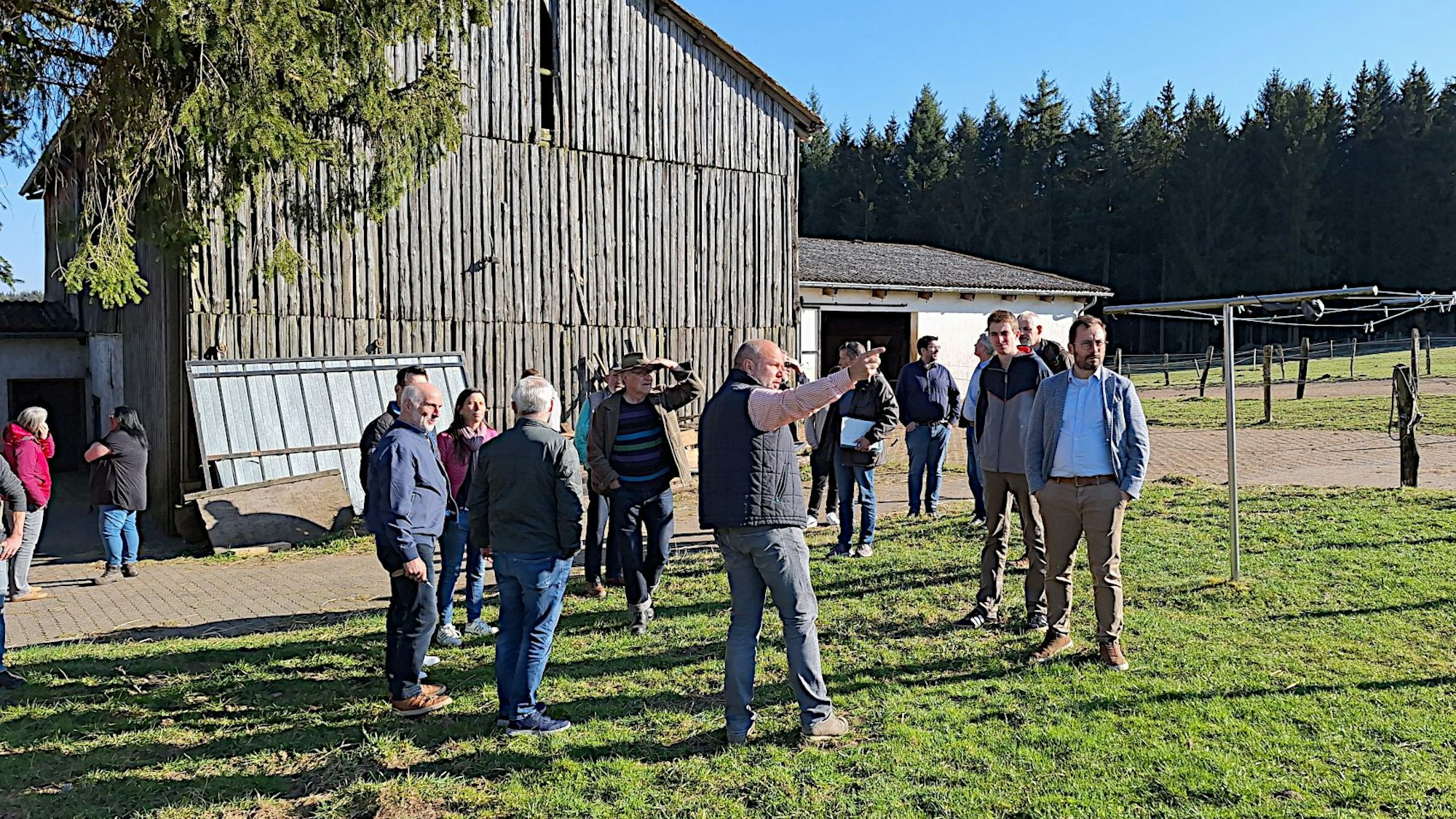Eine Gruppe steht auf einer Wiese und schaut sich ein Gebiet an, auf dem in der Gemeinde Dahlem ein Solarpark geplant werden soll.