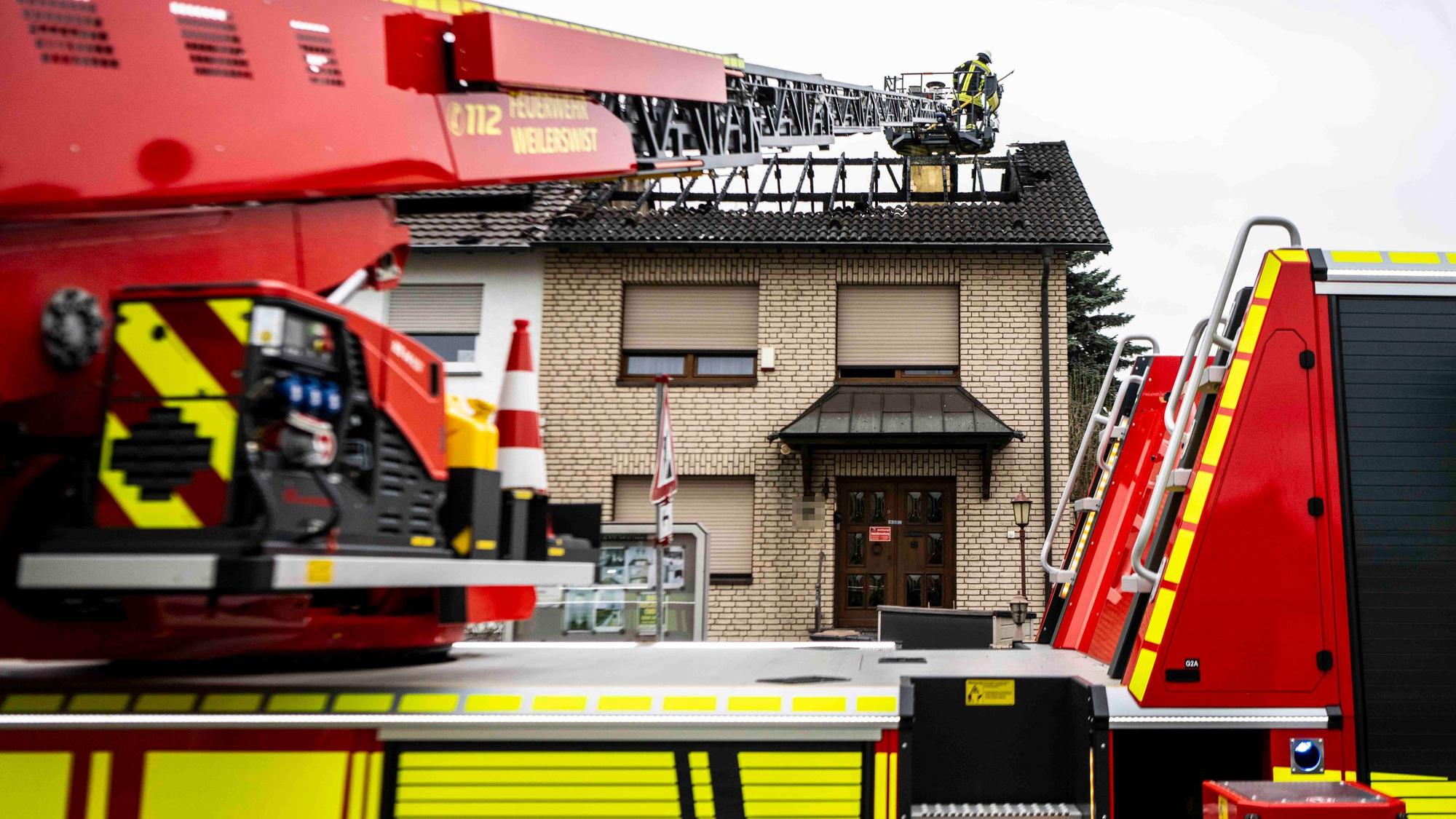 Das Bild zeigt den ausgebrannten Dachstuhl und die Drehleiter der Weilerswister Feuerwehr. Ein Feuerwehrmann schaut nach Glutnestern.