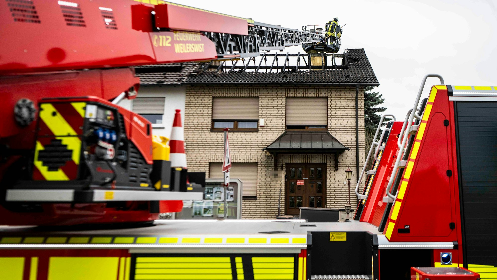 Das Bild zeigt den ausgebrannten Dachstuhl und die Drehleiter der Weilerswister Feuerwehr. Ein Feuerwehrmann schaut nach Glutnestern.
