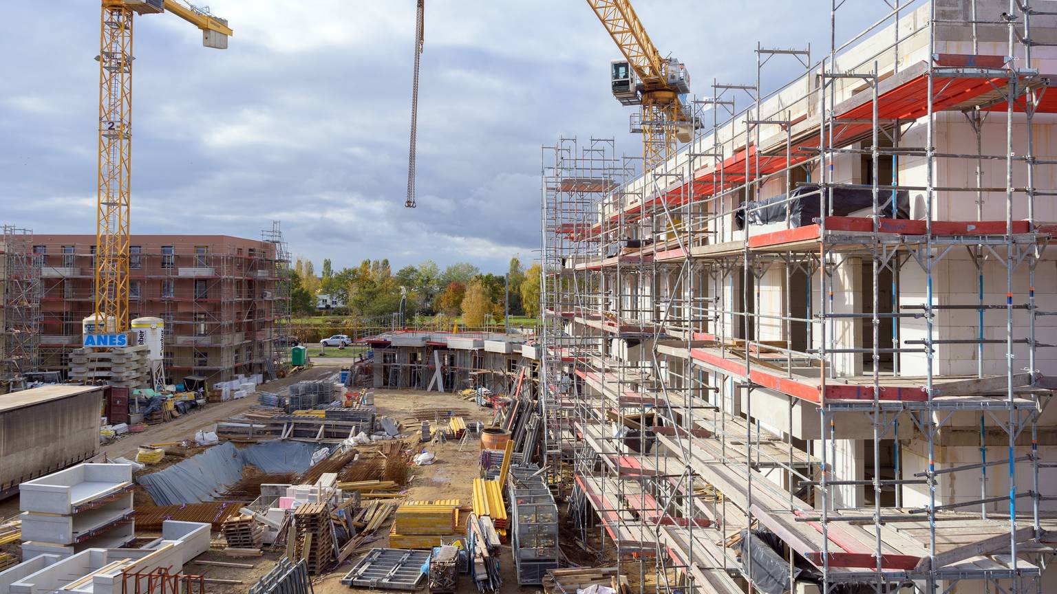 Gerüste stehen auf einer Baustelle an Rohbauten von Häusern. (Symbolbild)