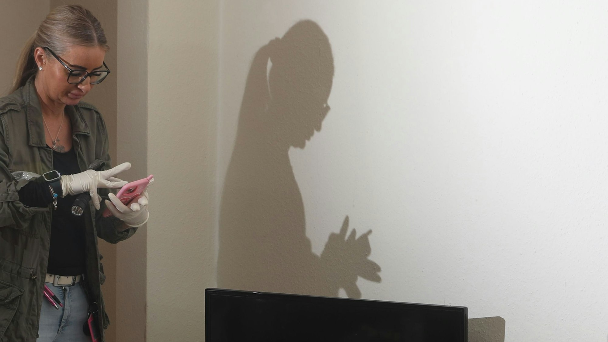 31.03.2025, Köln: Kommissrin Kristin macht am Einsatzort Beweisaufnahmen mit ihrem Handy. An eine Wand wird ihr Schatten geworfen.