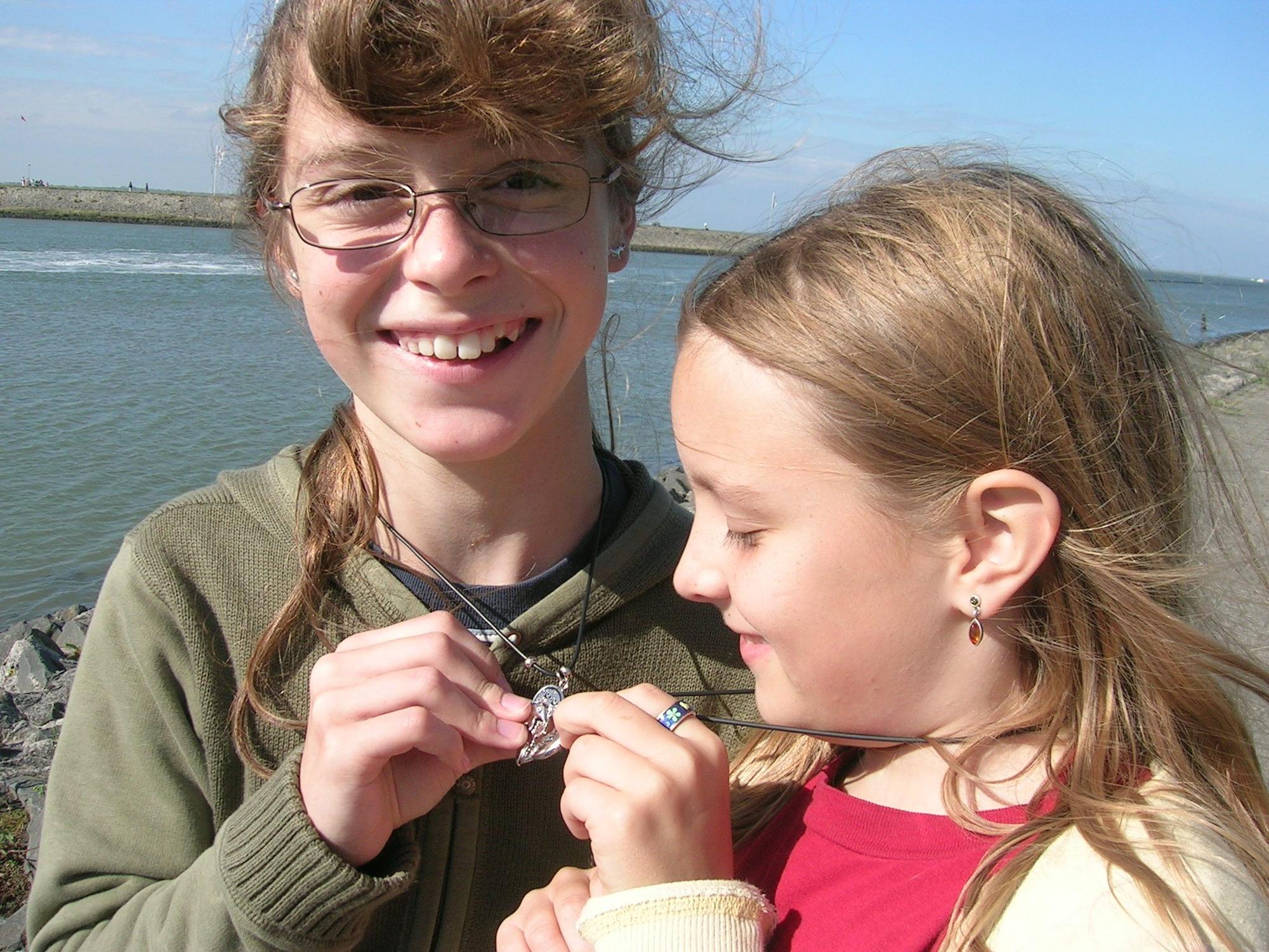 Auf dem Foto sind Miriam (l.) und Judith im Kindesalter zu sehen. Die beiden Mädchen halten Anhänger von Halsketten aneinander.