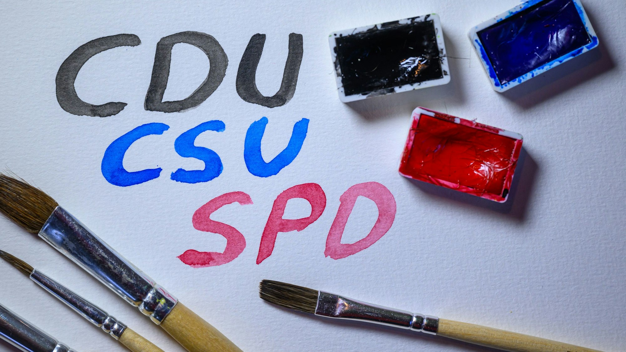 Mit Wasserfarben stehen die Namen der Parteien CDU/CSU und SPD auf einem Blatt Aquarellpapier.