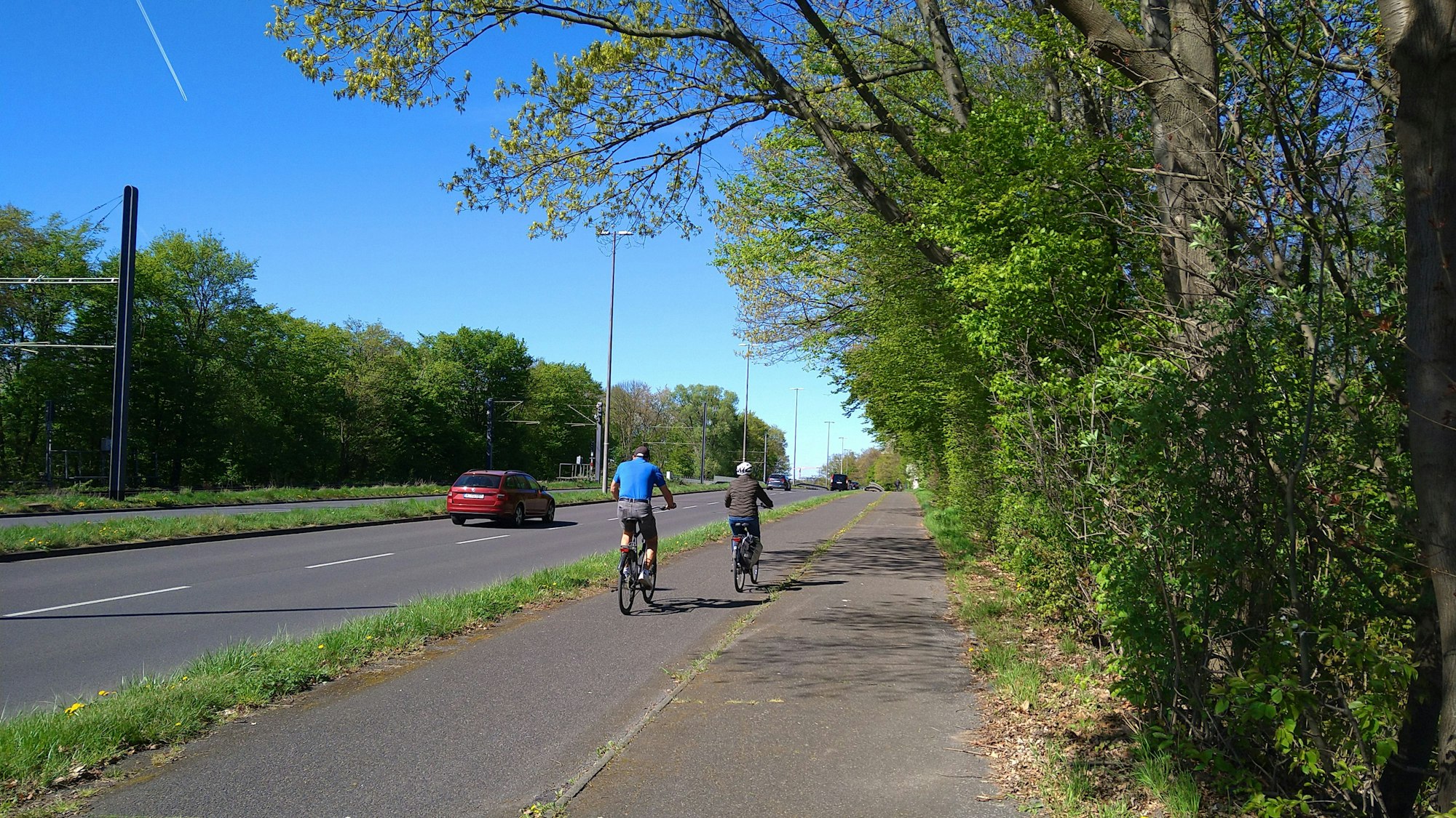 Radfahrer fahren auf einem Radweg. Daneben ist eine zweispurige Autostrecke.