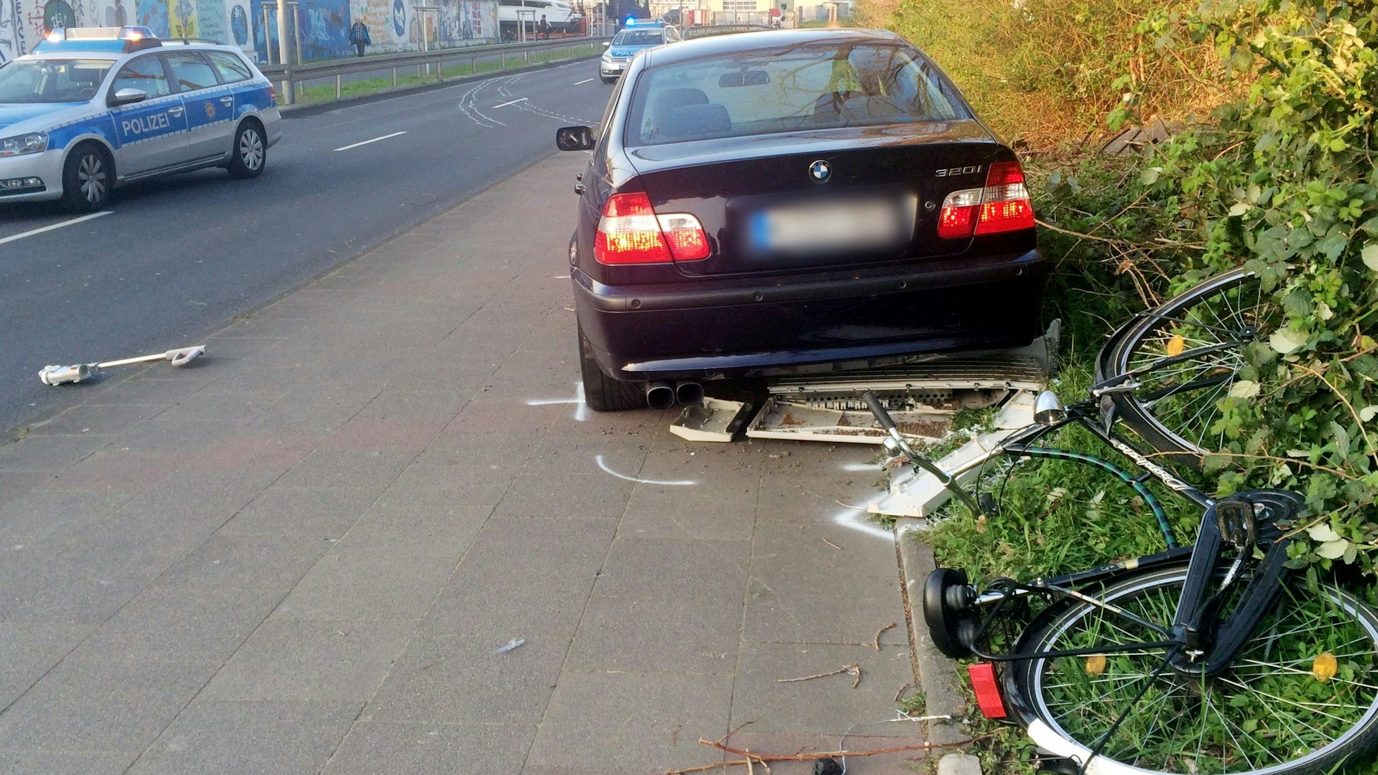 Ein Auto mit verpixeltem Kennzeichen steht dich neben einem Gebüsch auf einem Radweg, rechts davon liegt ein umgekipptes Fahrrad.
