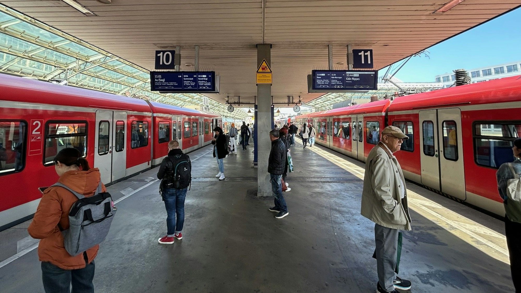 S-Bahnen fahren im Kölner Hauptbahnhof ein, am Gleis warten Leute.