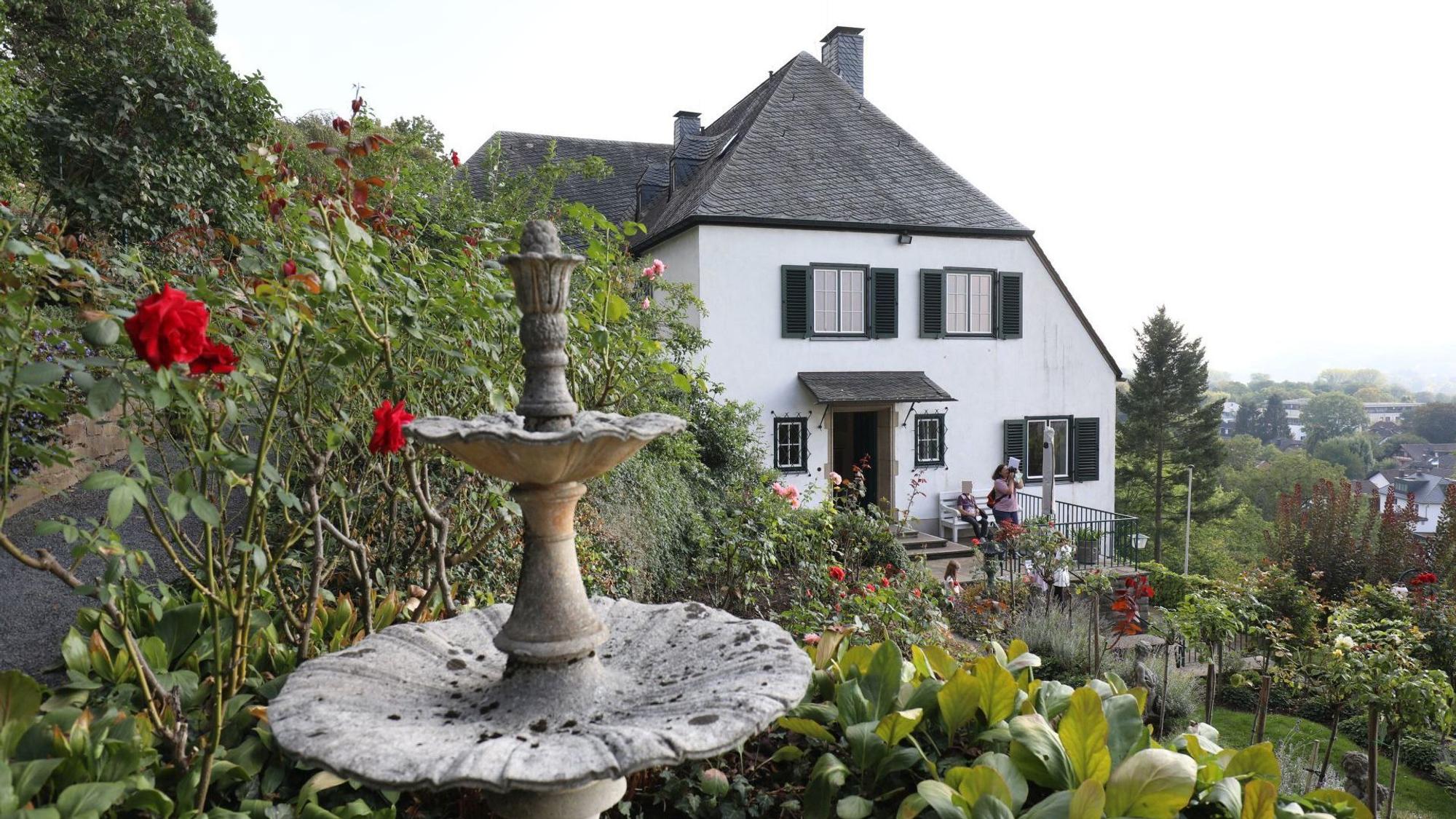 Ein Wohnhaus mit weißer Fassade und grünen Fensterläden, im Vordergrund Rosen in einem großen Garten.