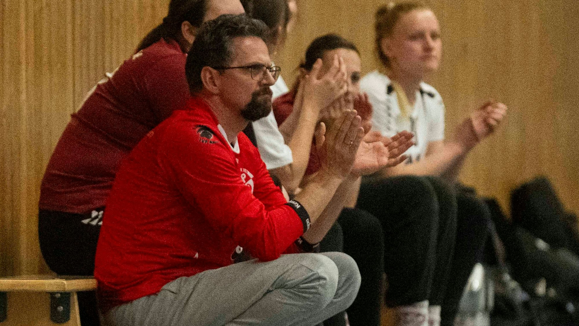 Ein Mann, der Brille trägt, klatsch in der Hocke in die Hände.