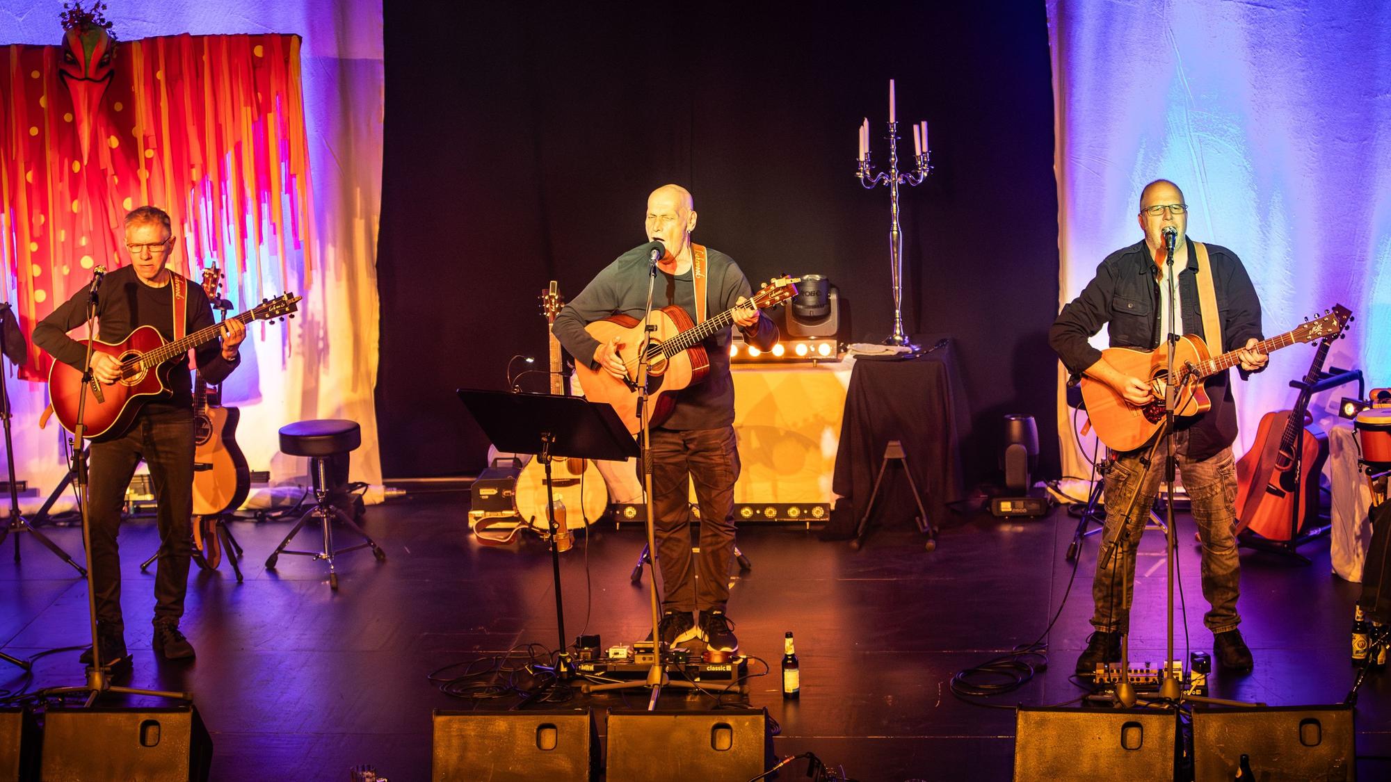 Die drei Bandmitglieder stehen auf der Bühne und performen.