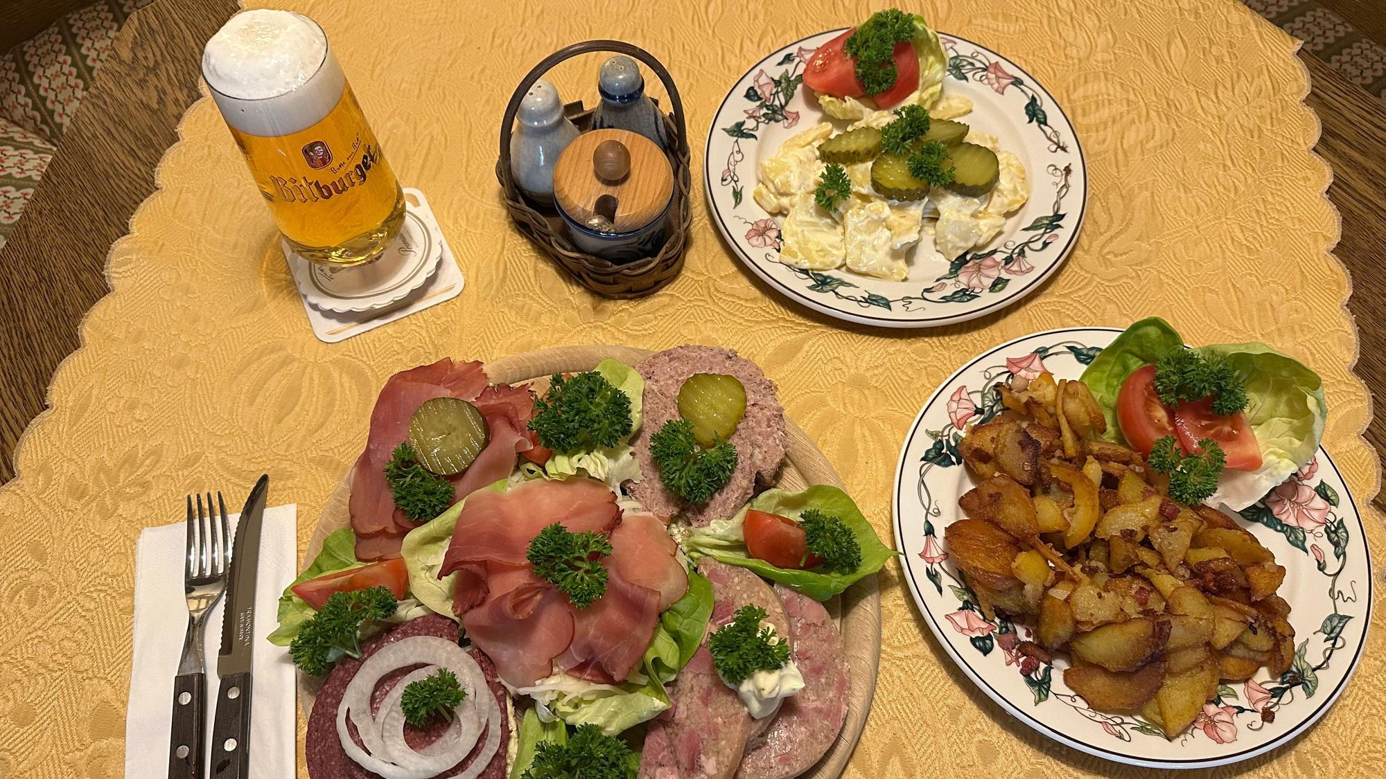 Vorne der Dorfkrug Teller für 22 Euro, rechts eine Portion Bratkartoffeln, hinten der selbstgemachte Kartoffelsalat, dazu ein Bitburger Pils für 0,2 Liter für 2,20 Euro.