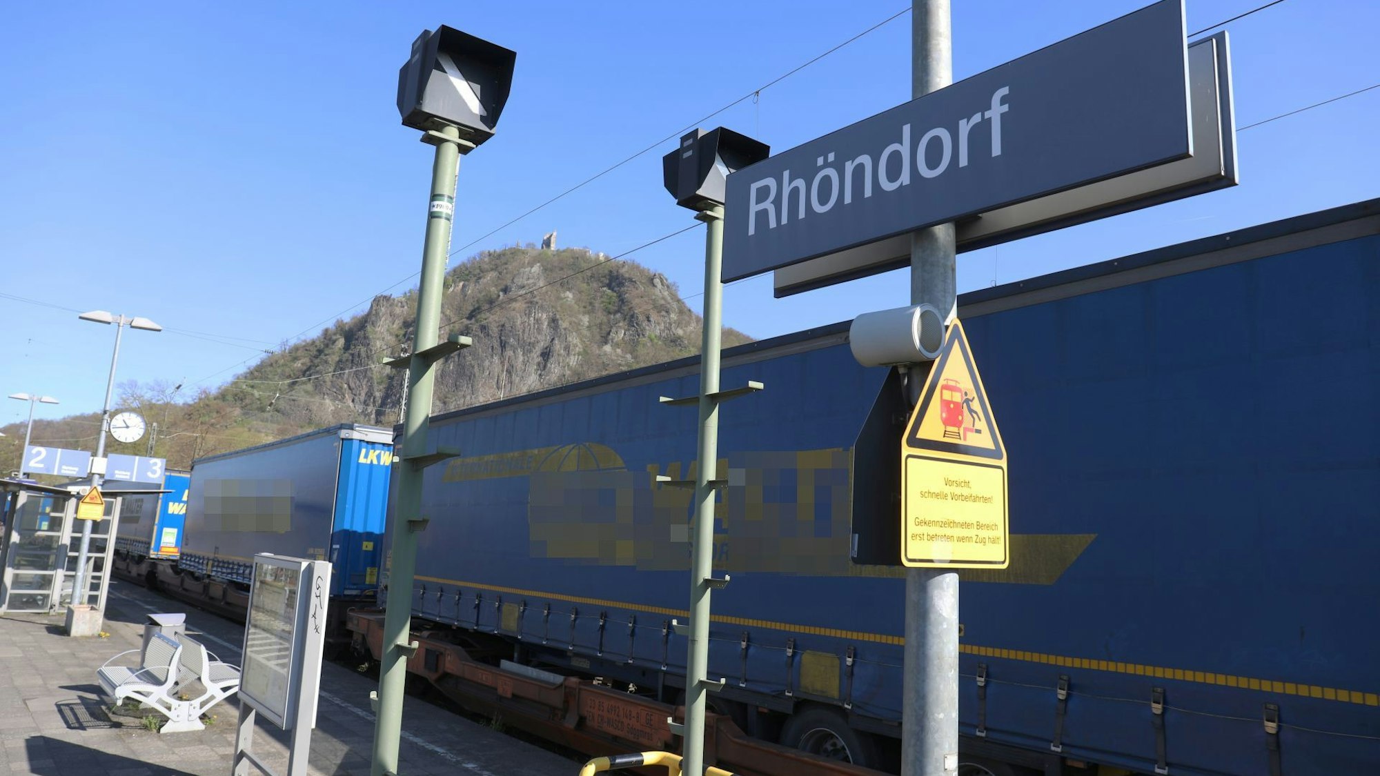Ein Güterzug fährt durch den Bahnhof Rhöndorf, im Hintergrund der Drachenfels.