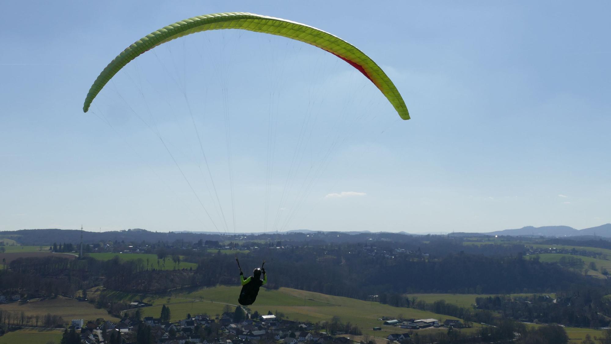 Eine Person fliegt mit einem Gleitschirm über das Siegtal.