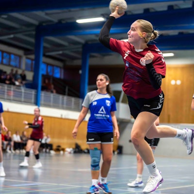 Eine junge Frau setzt mit einem Handball in der rechten Hand zum Wurf an.