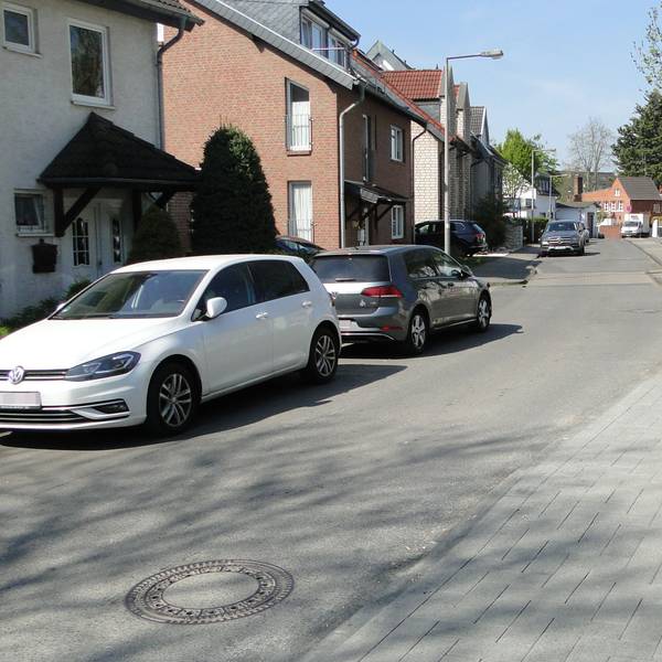Auf einer schmalen Fahrbahn in einem Wohngebiet parken Autos am Straßenrand