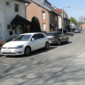 Auf einer schmalen Fahrbahn in einem Wohngebiet parken Autos am Straßenrand