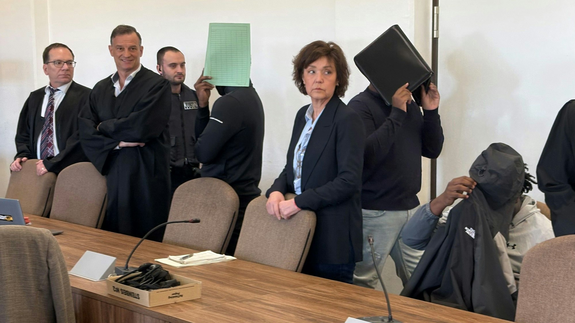 Die drei Angeklagten mit Verteidigern, Dolmetscherin und Wachtmeister beim Prozess im Kölner Landgericht