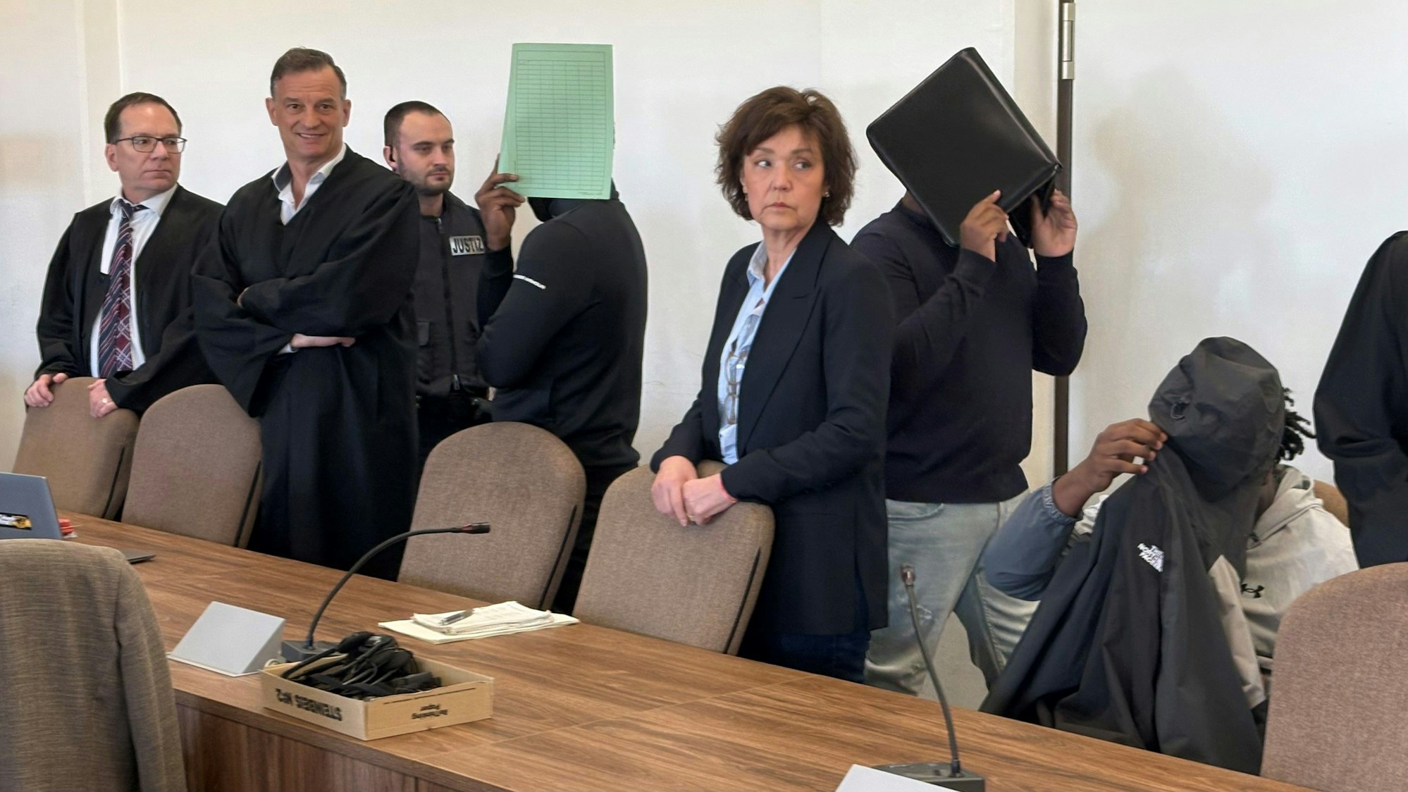 Die drei Angeklagten mit Verteidigern, Dolmetscherin und Wachtmeister beim Prozess im Kölner Landgericht.