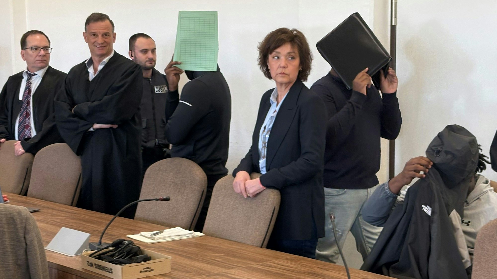 Die drei Angeklagten mit Verteidigern, Dolmetscherin und Wachtmeister beim Prozess im Kölner Landgericht