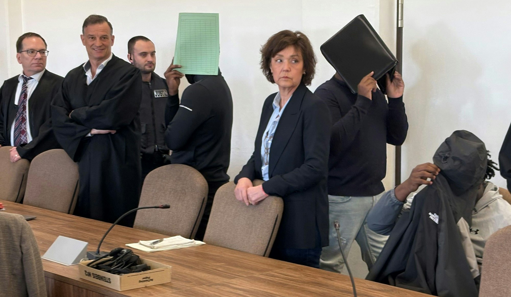 Die drei Angeklagten mit Verteidigern, Dolmetscherin und Wachtmeister beim Prozess im Kölner Landgericht.
