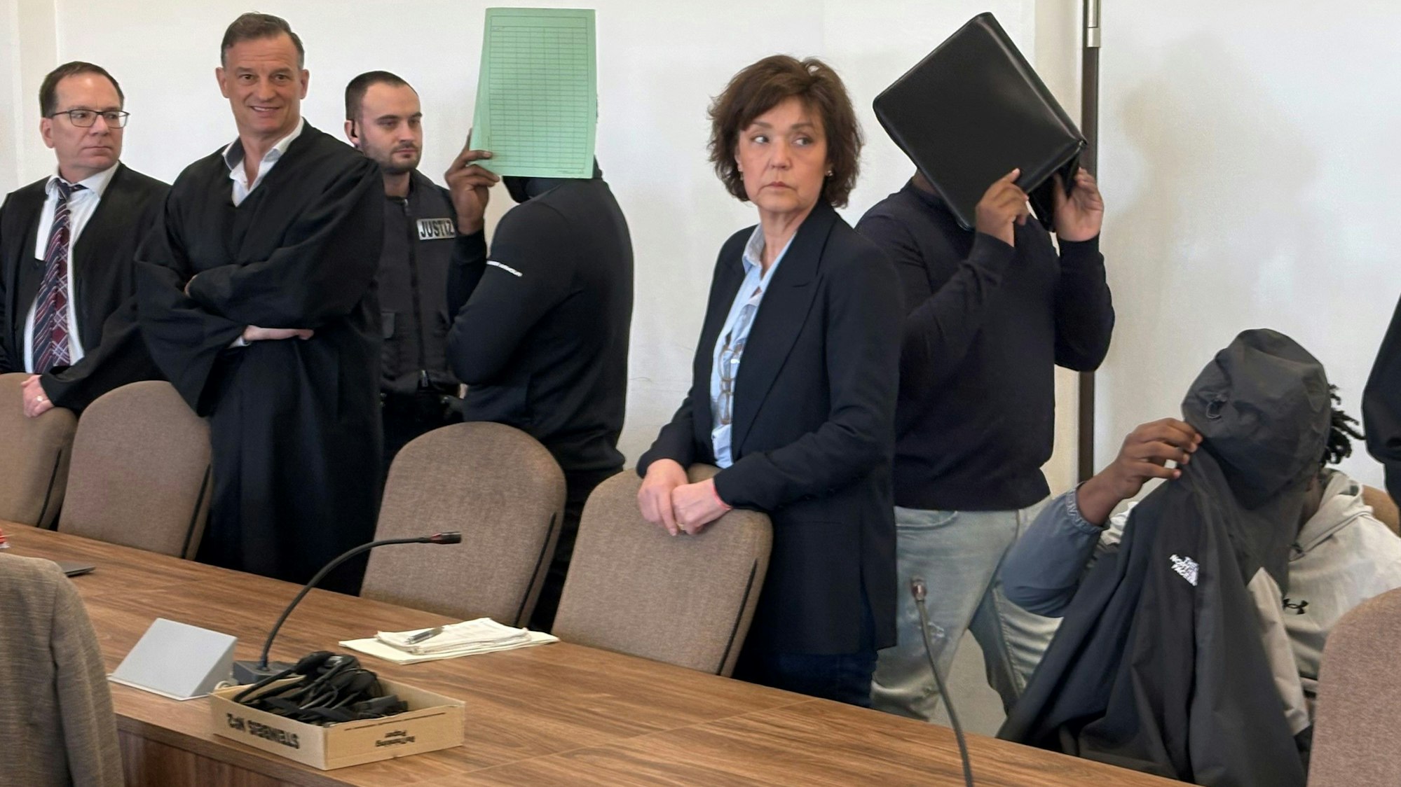 Die drei Angeklagten mit Verteidigern, Dolmetscherin und Wachtmeister beim Prozess im Kölner Landgericht