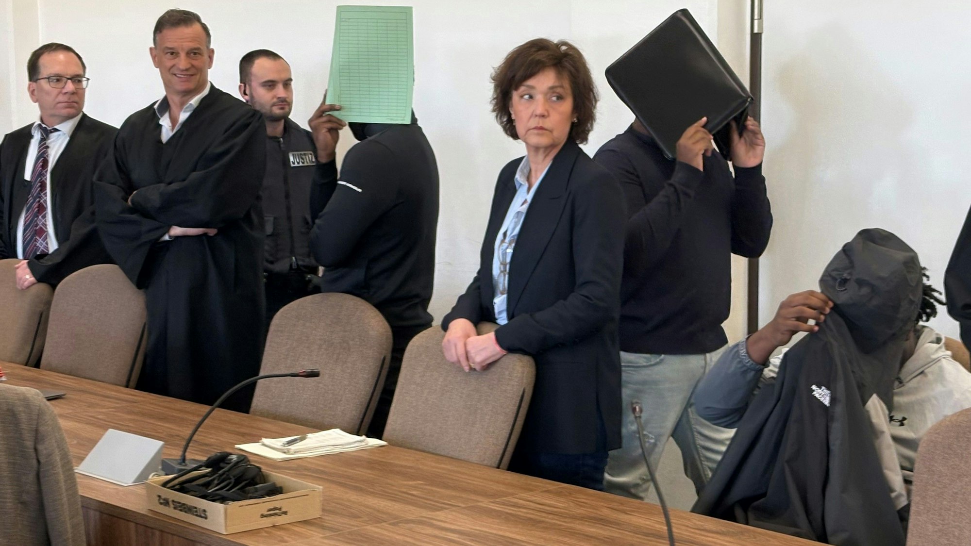 Die drei Angeklagten mit Verteidigern, Dolmetscherin und Wachtmeister beim Prozess im Kölner Landgericht