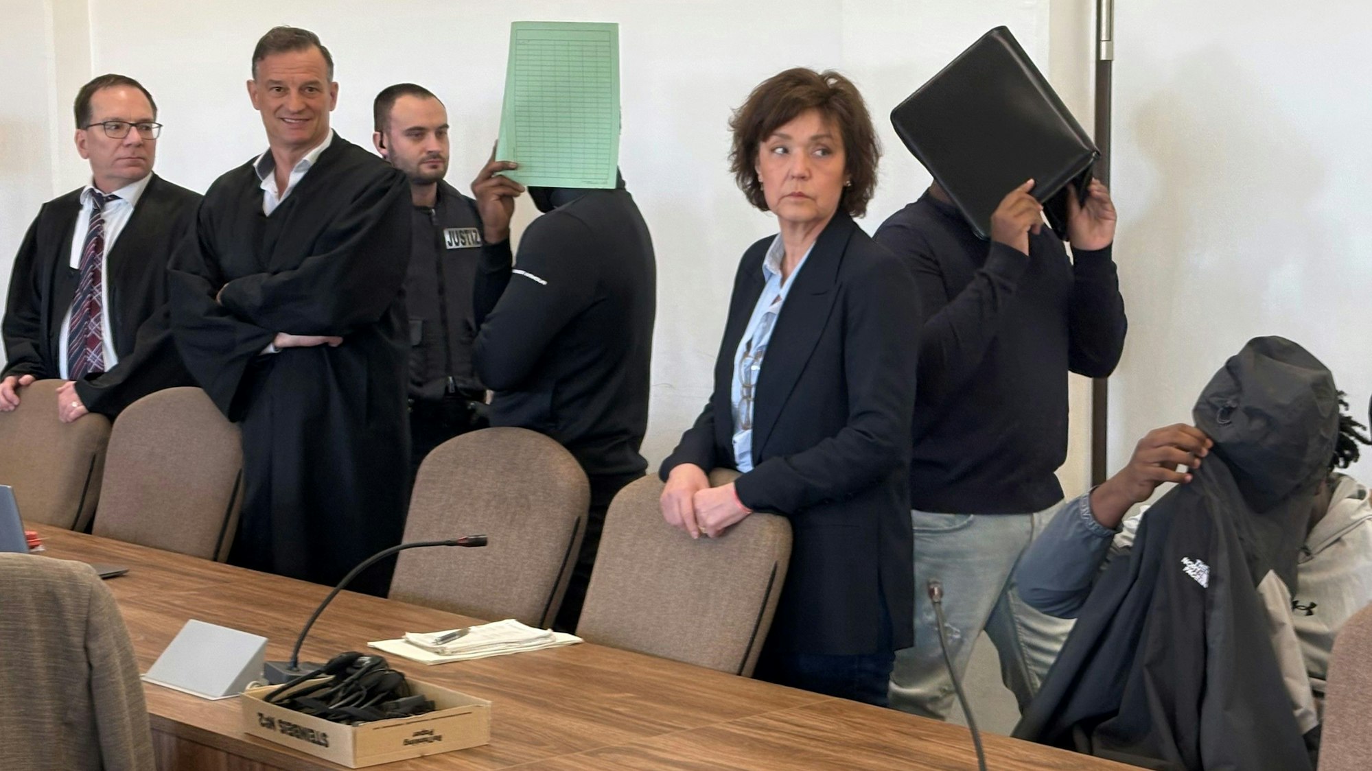 Die drei Angeklagten mit Verteidigern, Dolmetscherin und Wachtmeister beim Prozess im Kölner Landgericht