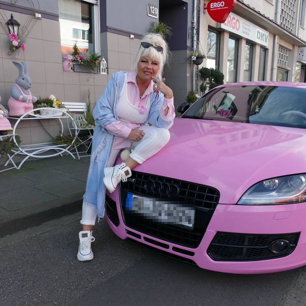 Heike Kleindienst, gekleidet in rosa und weiß, sitzt halb auf ihrem rosa Audi und lächelt. Hinter ihr sind rosa Häschendekorationen auf weißen Stühlen vor ihrem Haus platziert.