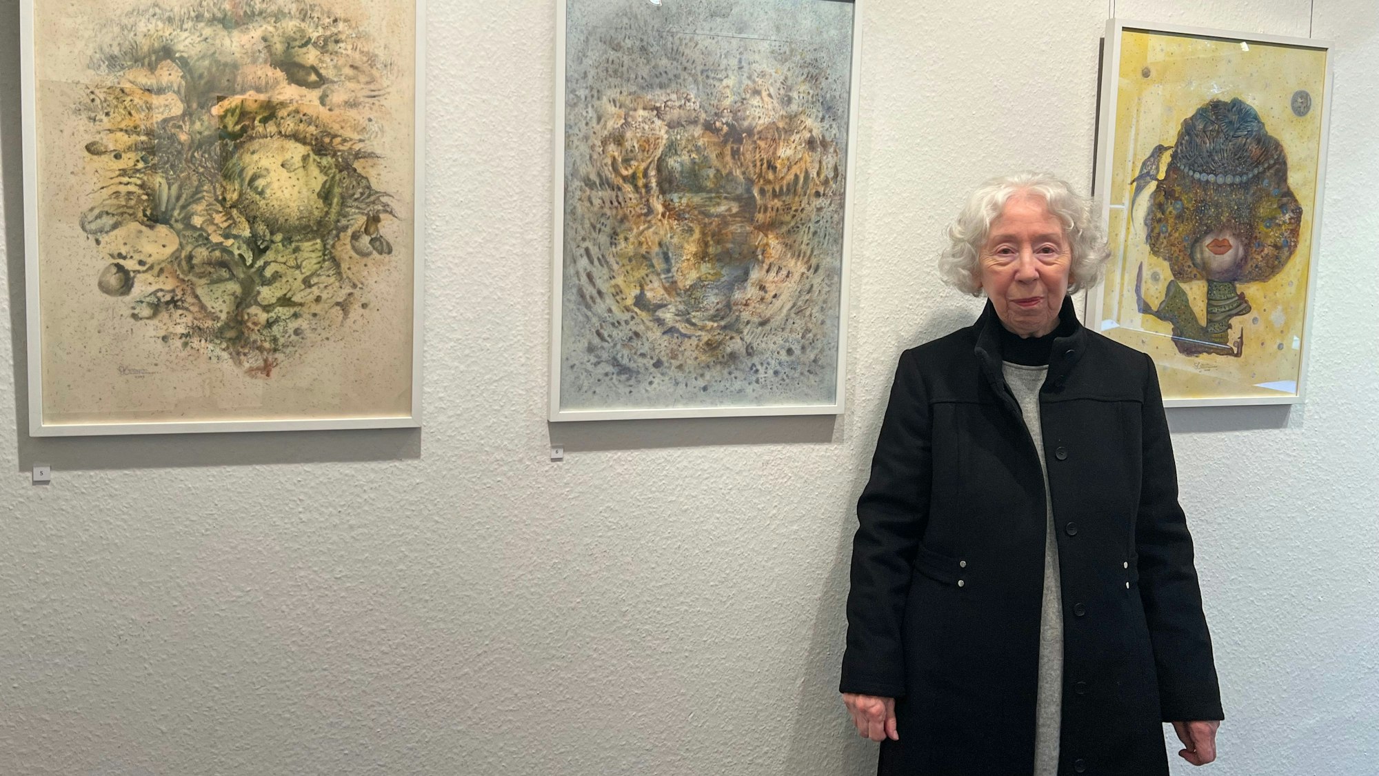 Eine Frau steht vor ihren Bildern.