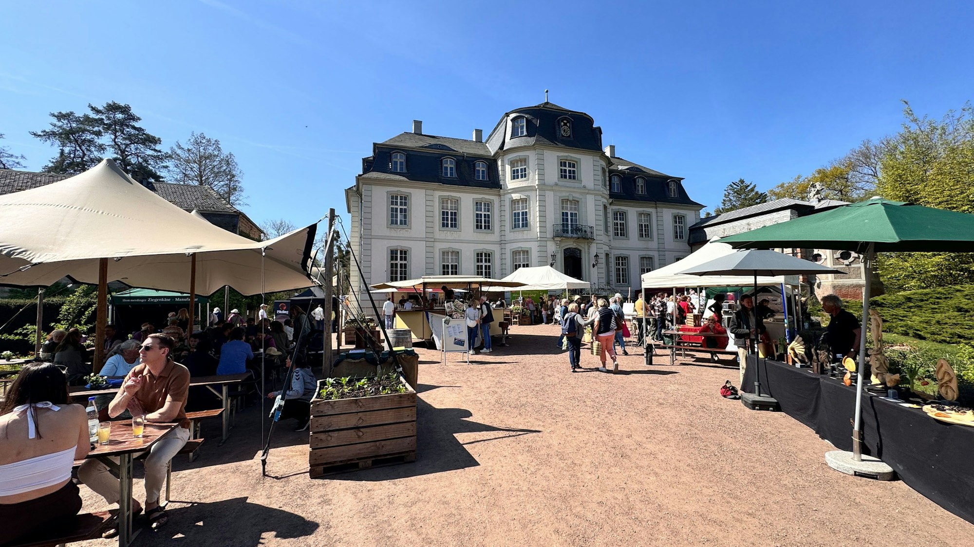 Von Sonnenschirmen geschützte Stände, im Hintergrund ein Schloss mit einer hellen Fassade.