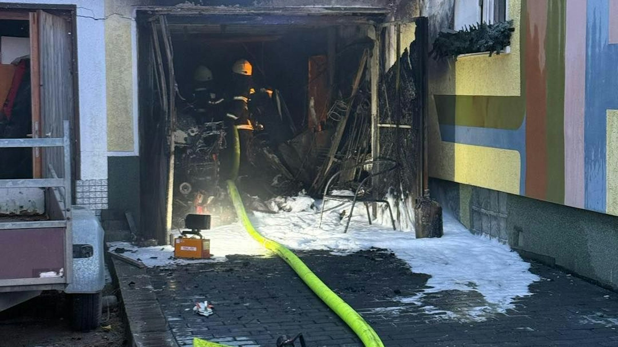 Ein Feuerwehrmann löscht mit einem gelben Schlauch den Garagenbrand.