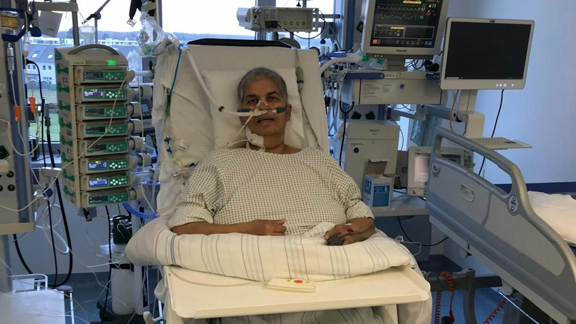 Oya Kar sitzt in einem Liegestuhl auf der Intensivstation. Aus ihrer Nase und ihrem Hals ragen Schläuche, um sie herum leuchten Geräte.