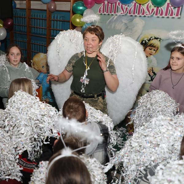 Eine Ordensschwester steht mit Engelsflügeln und Heiligenschein inmitten von ukrainischen Kindern.
