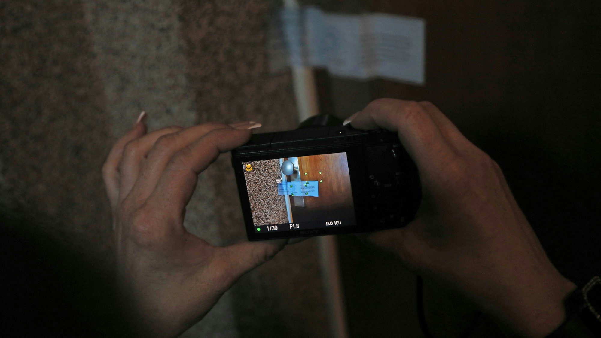 30.03.2025, Köln: Zwei Hände halten eine Kamera, mit der die Versiegelung einer Wohnungstür dokumentiert wird.