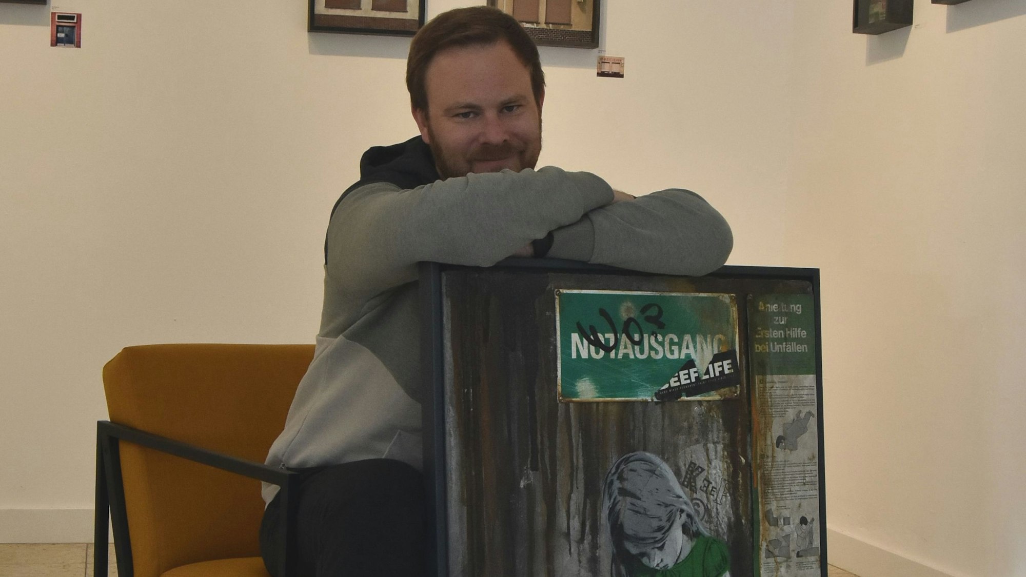 Ein Mann sitzt auf einem senfgelben Sessel und lehnt sich auf ein Graffiti-Werk.