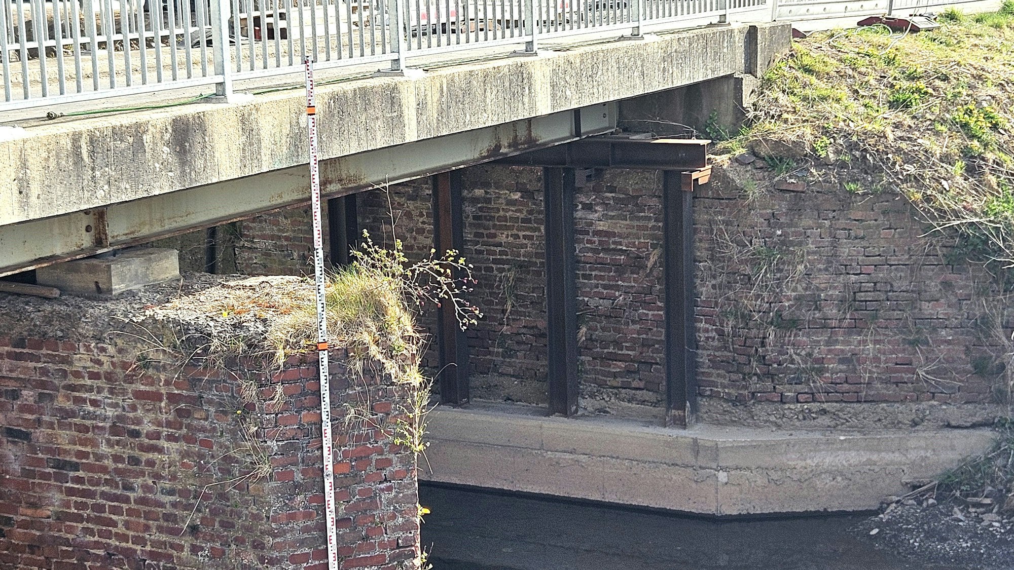 Blick auf den Bereich unter der Brücke mit Betonfundament und Eisenträgern.