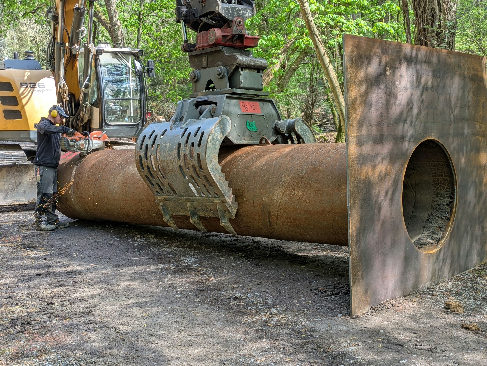Ein Arbeiter kürzt das Rohrstück mit Schild, hinter dem sich das Bachwasser während der Bauarbeiten stauen soll.