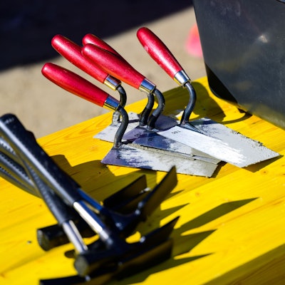 Maurerhammer und Maurerkellen liegen auf einer Baustelle.