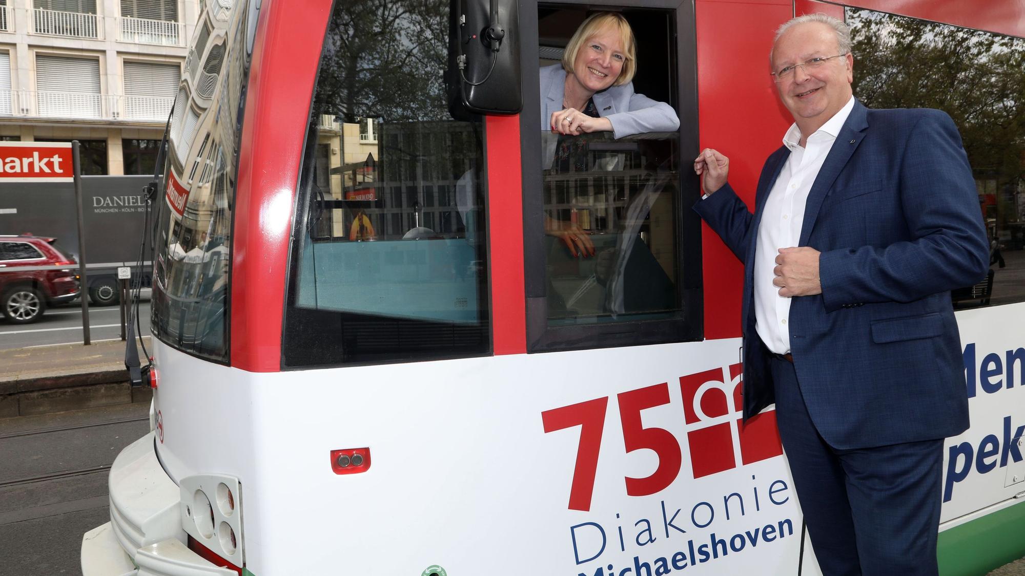 Zu sehen ist auf der linken Seite Stefanie Haaks, Vorstandsvorsitzende der KVB, die aus dem Fenster der Fahrerkabine einer Bahn der KVB herausschaut. Auf der rechten Seite ist Uwe Ufer zu sehen, der neben der Bahn steht.