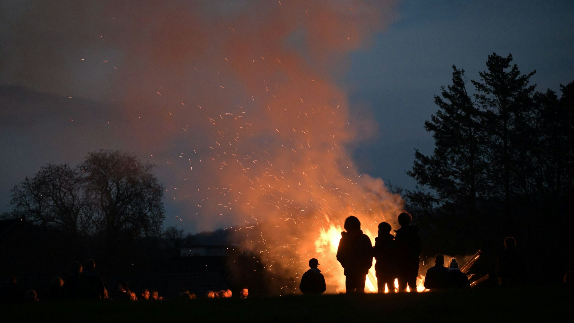 Bei Nacht steht eine Gruppe Menschen vor dem Osterfeuer auf dem Hofferhof in Hoffnungsthal.