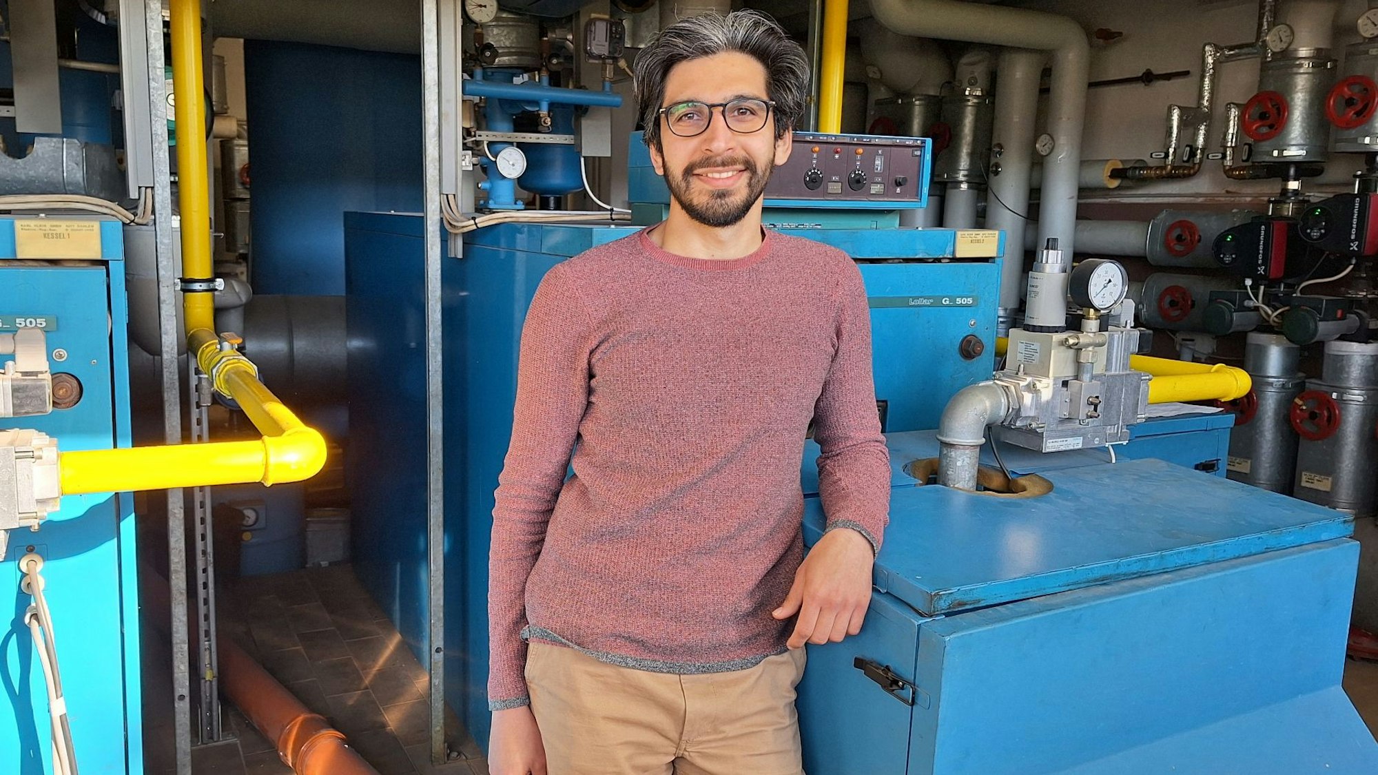 Der Energiemanager Nima Haghighatian lehnt sich mit dem Ellbogen an die Heizungsanlage der Grundschule in Dahlem.