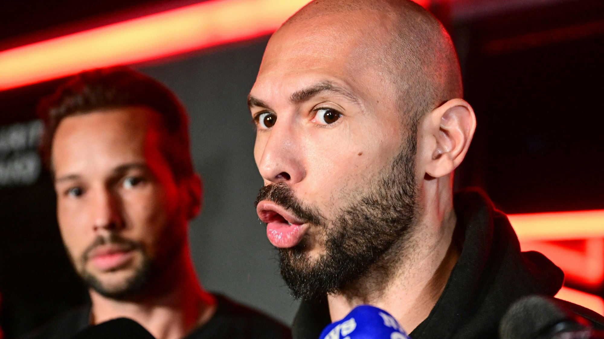 Andrew Tate (R) and his brother Tristan (L) speak to the media as they arrive in Romania back from US, in Bucharest March 22, 2025. Self-described misogynist influencer Andrew Tate return to Romania, where he is facing rape and human trafficking charges, after a trip to the US. The British-American figurehead of the online masculinist movement travelled to Florida, together with his brother, last month, marking the first time he had been out of the eastern European country since his 2022 arrest. Under judicial supervision, the Tates need to report to authorities on March 24, a no-show potentially leading to "preventive arrest", according to Romanian authorities. (Photo by Daniel MIHAILESCU / AFP)