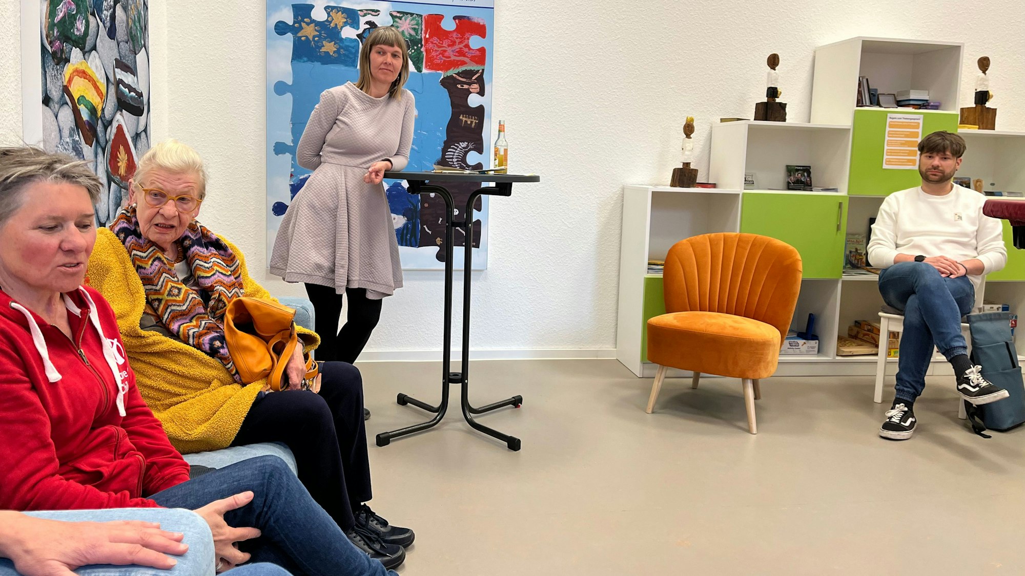 Eine stehende Frau und drei sitzende Personen diskutieren.