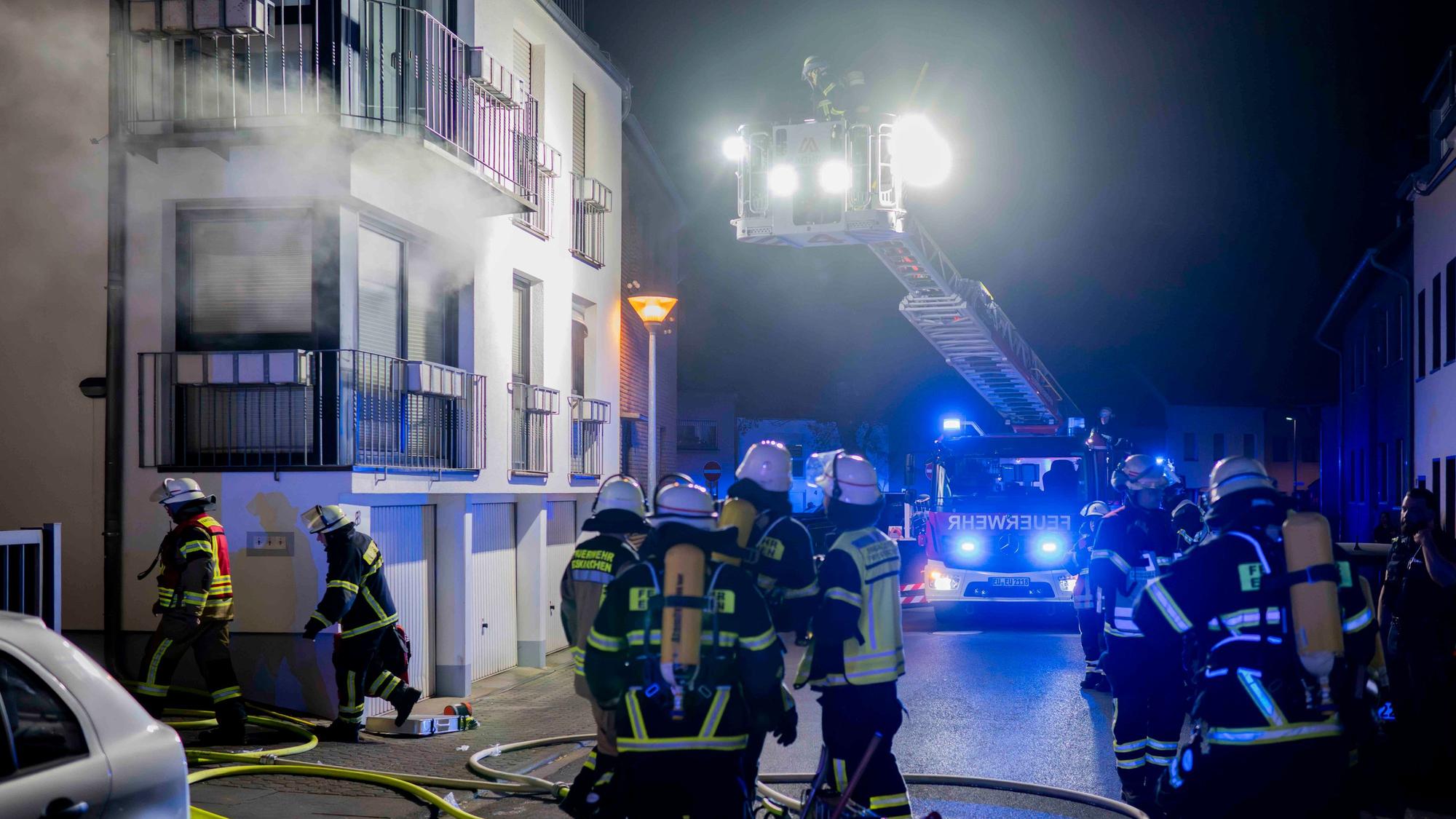 Feuerwehrleute stehen vor einem Haus in Euskirchen. Aus einem Raum im ersten Obergeschoss eines Hauses dringt Rauch.