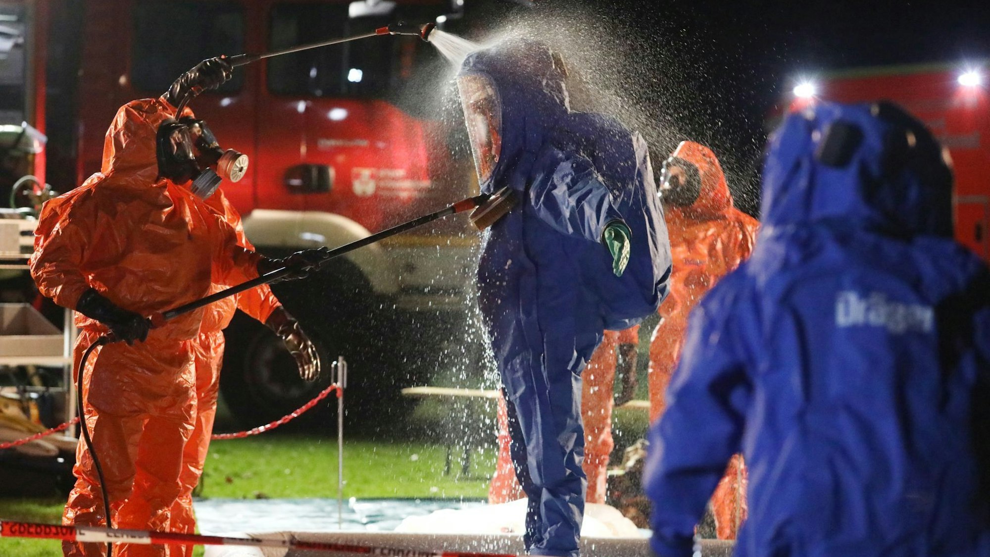 Feuerwehrleute in roten und blauen Schutzanzügen, im Hintergrund ein Einsatzfahrzeug der Feuerwehr