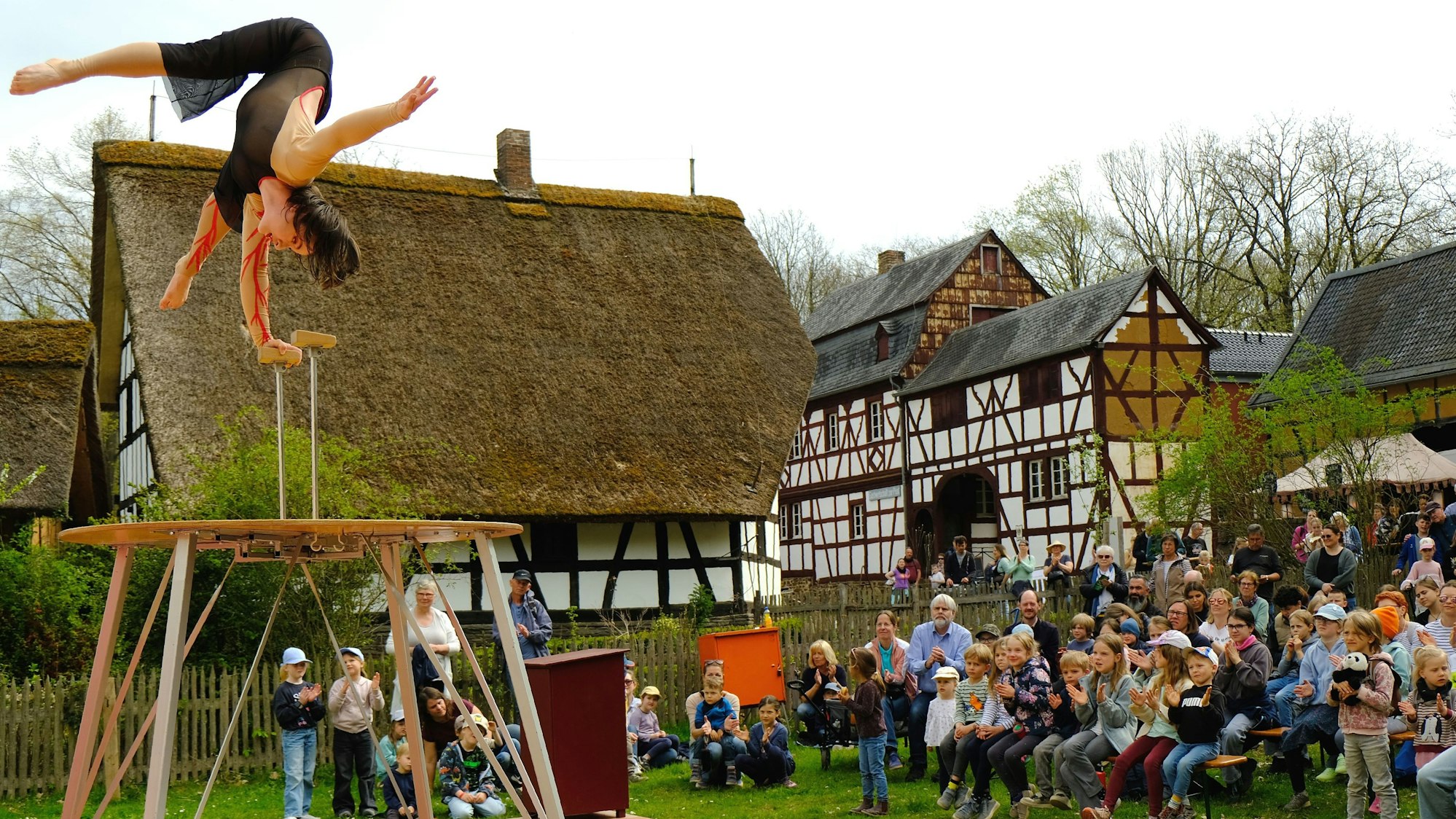 Die Artistin Joana Lokaichuk tritt mit ihrer Handstand-Nummer in der Freiluftarena des „Jahrmarkt anno dazumal“ auf. Im Hintergrund sind historische Fachwerkbauten und Jahrmarkt-Besucher zu sehen.