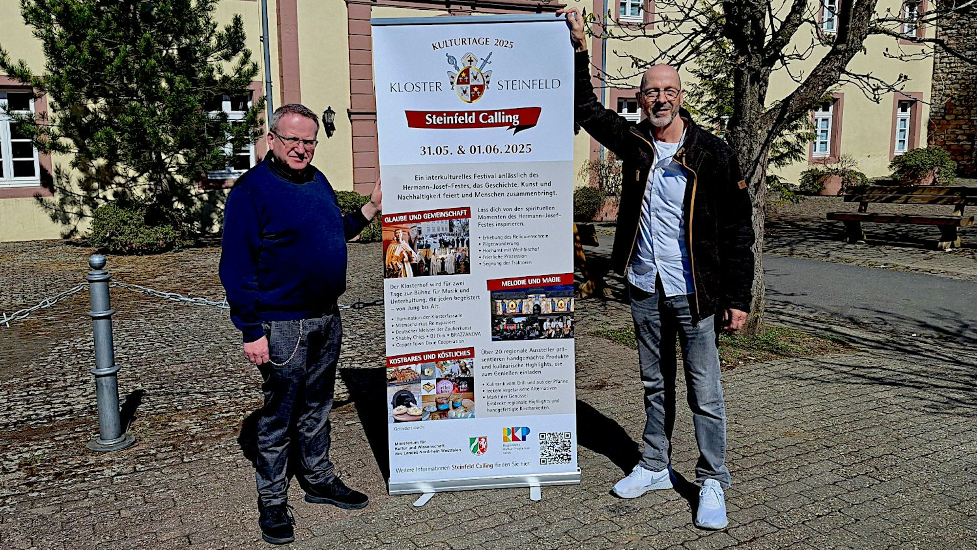 Zwei Männer, P. Lambertus Schildt und Martin Reinicke, stehen im Innenhof des Klosters Steinfeld an einem Plakat, das auf die Veranstaltungsreihe „Steinfeld Calling“ hinweist.